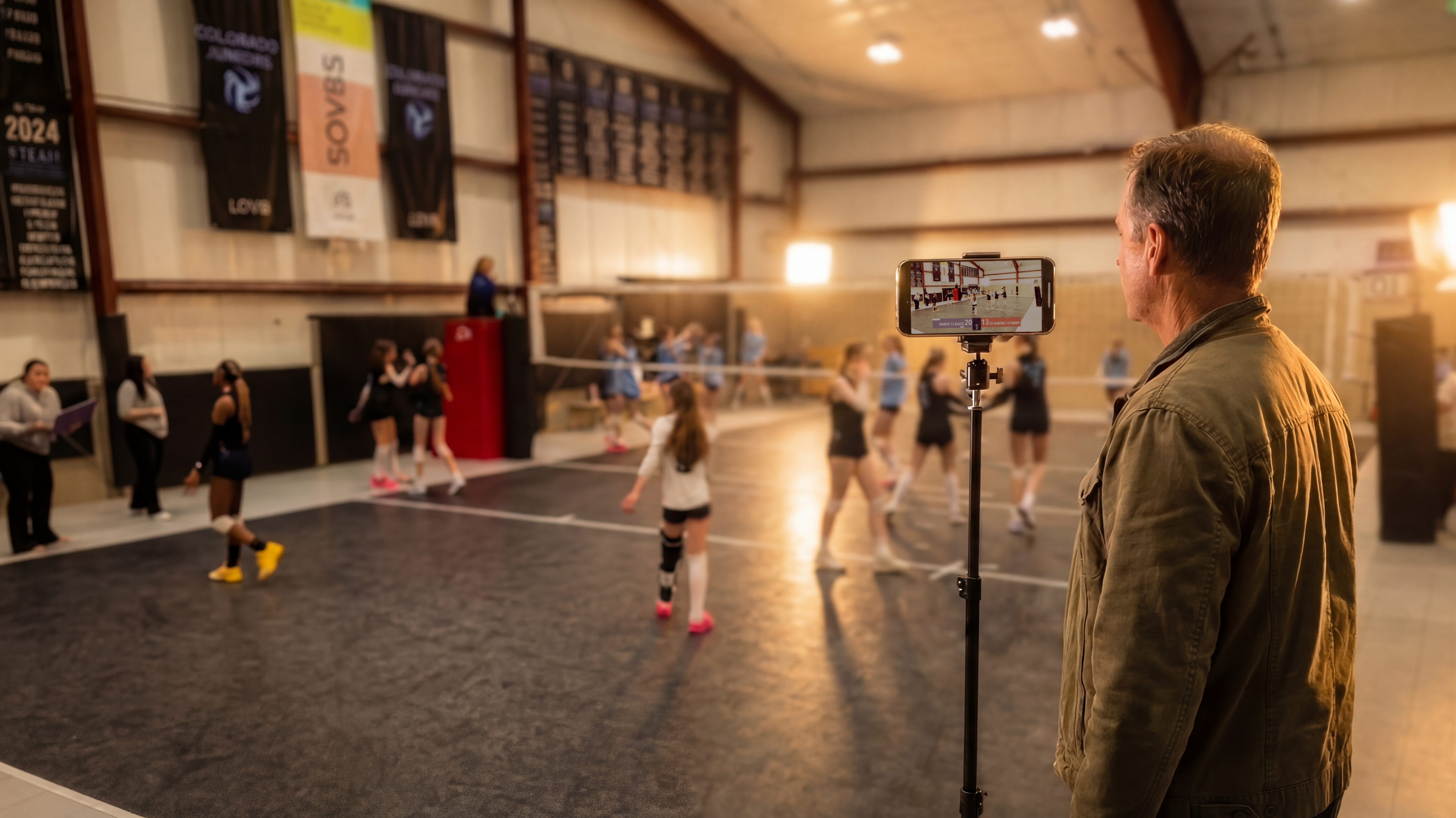 Ouder die een jeugdvolleybalwedstrijd filmt in een sporthal met CineSportCam op een telefoon op een statief.