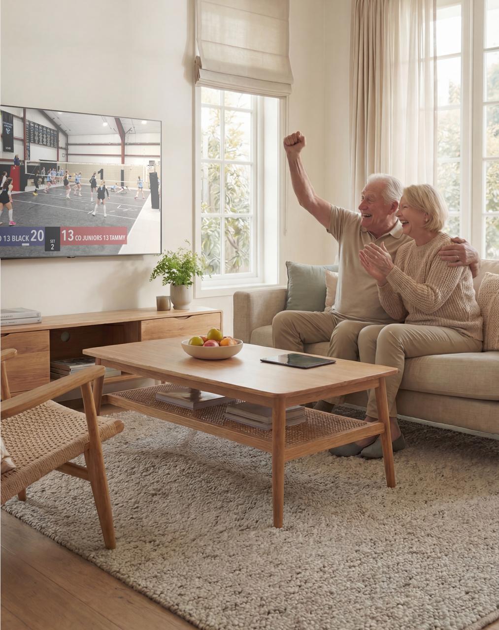 Grandparents cheering at home while watching a youth volleyball game streamed live on their TV.